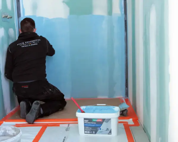 Un carreleur applique une protection étanche avant la pose carrelage dans une douche.