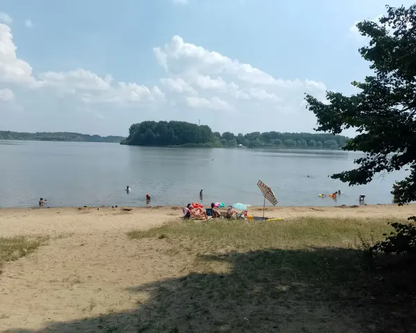 Na Jeziorze Przeczyckim można się kąpać. Ludzie odpoczywają na plaży i pływają w wodzie.