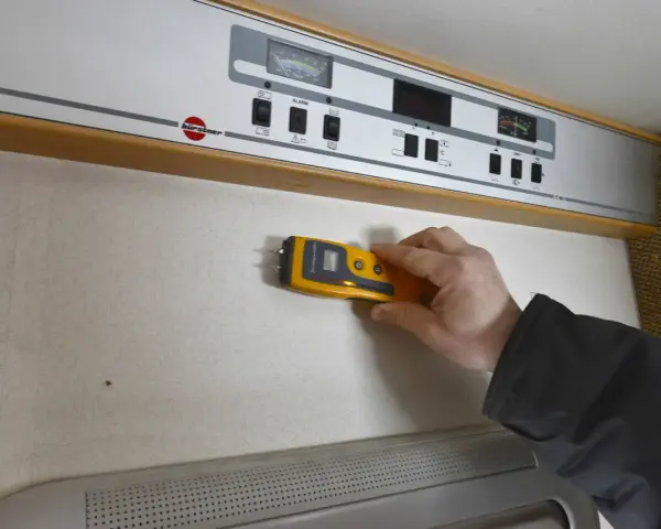 Hand håller fuktmätare mot vägg för fukttest protokoll.