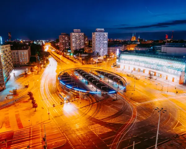 Widok z lotu ptaka na nocne miasto z długimi smugami świateł samochodowych i tramwajowych.