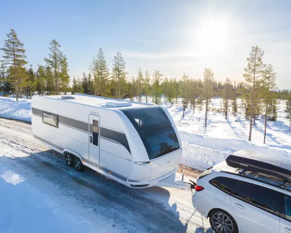 Vit husvagn dras av bil genom snöig skog. Den bästa husvagnen för äventyr nära Haparanda.