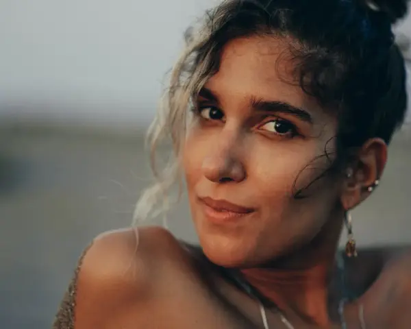 Photos de portrait d'une jeune femme aux cheveux bouclés, le sable sur son épaule, regardant la caméra avec un léger sourire.