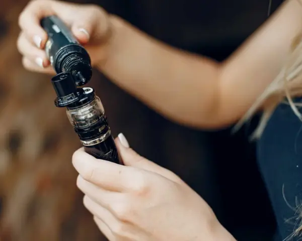Manos rellenando un vaporizador con líquido de nicotina salina.
