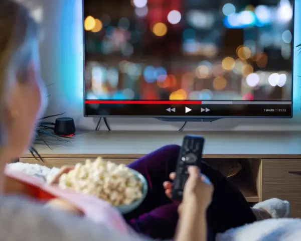 Persona relajada viendo una serie en francés en la televisión, con palomitas y mando a distancia.