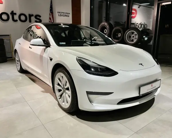 Biała Tesla Model 3 z napędem na cztery koła stoi w salonie samochodowym.