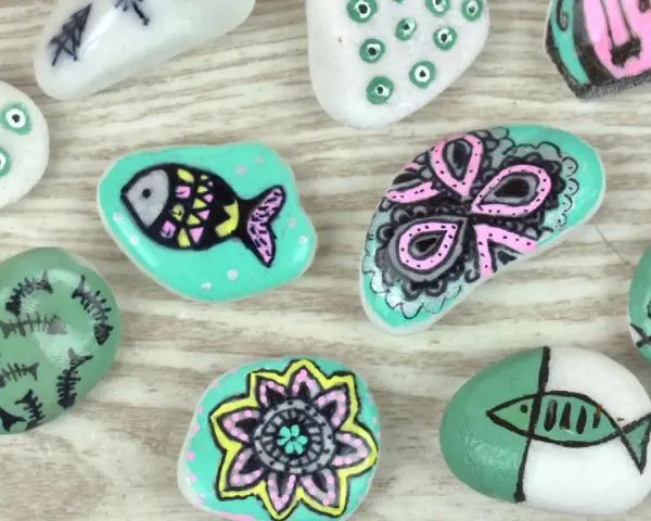Ideas para pintar piedras de playa: peces, flores y diseños abstractos en tonos turquesa, blanco y rosa.