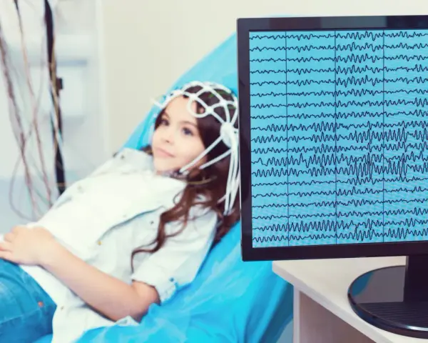 Dziewczynka z czepkiem EEG leży na kozetce, a na monitorze widać zapis fal mózgowych. Badanie pomaga zrozumieć zespół Aspergera a wynik EEG.