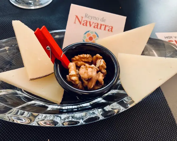 Queso en cuñas con nueces en un cuenco negro, sobre plato de cristal y tarjeta "Reino de Navarra".