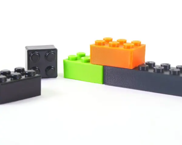 Klocki z drukarki 3D, wykonane z materiału ABS, w kolorach czarnym, zielonym i pomarańczowym, ułożone na białym tle.