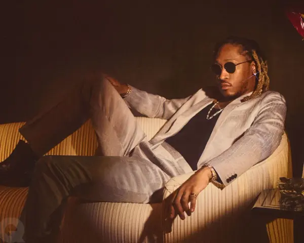 Ein Hip-Hop-Künstler in einem schicken Anzug entspannt sich auf einem Sofa, trägt Sonnenbrille und Schmuck.