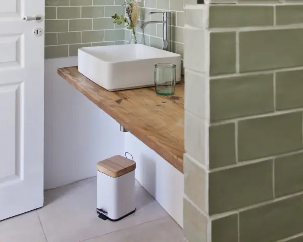 Plan de travail pour salle de bain avec lavabo carré, robinetterie moderne et poubelle design.