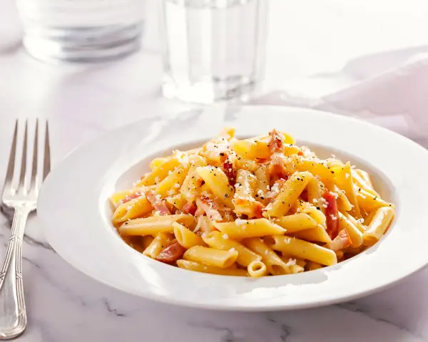 Piatto di pasta penne con speck e zafferano, guarnito con parmigiano e pepe nero.