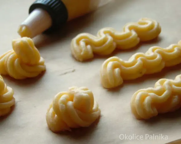 Kremowe eklery z czekoladą i profiteroles w trakcie przygotowania. Widać rękaw cukierniczy i wyciskane ciasto.