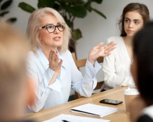 Kobieta w okularach, prezentująca kompetencje rady pedagogicznej, gestykuluje podczas spotkania.