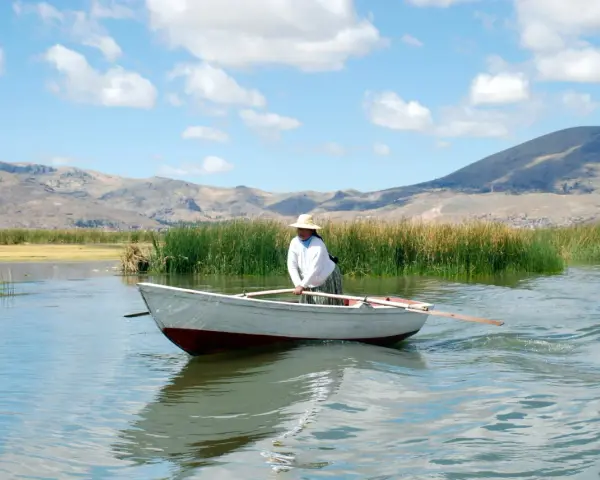 Donna con cappello di paglia rema su un lago, con montagne sullo sfondo. Mete agosto fuori Europa, un'immagine di pace.