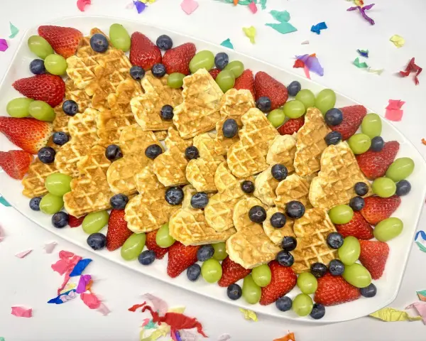 Herzförmige Waffeln mit Erdbeeren, Blaubeeren und grünen Trauben auf einem Teller – ein bunter obstteller kinder für jeden Anlass.
