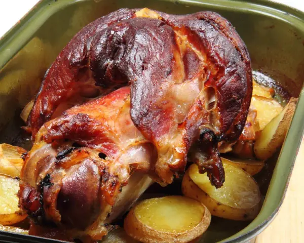 Pieczona golonka w zielonej brytfance, otoczona ziemniakami. Idealna marynata do golonki sprawiła, że skórka jest chrupiąca.