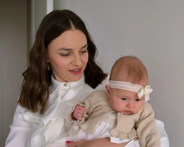 Elegancka mama z niemowlakiem. Inspiracja, jak ubrać się na chrzciny jako gość: biała koszula, subtelne dodatki.