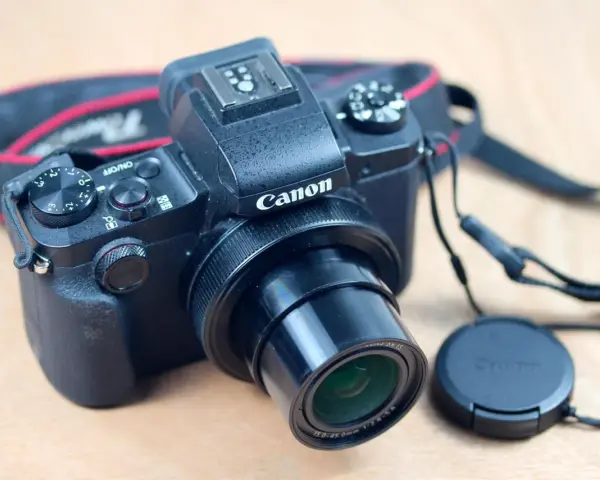 Un appareil photo noir Canon G1X Mark III, prêt pour un test. Courroie rouge et noire visible.