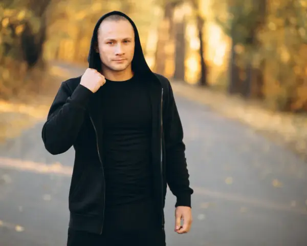 Mężczyzna w czarnej bluzie męskiej Guess z kapturem, stojący na ścieżce w jesiennym parku.
