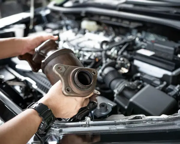 Mechanic holding a catalytic converter, ready for replacement. Understanding the catalytic converter replacement cost is key for car owners.