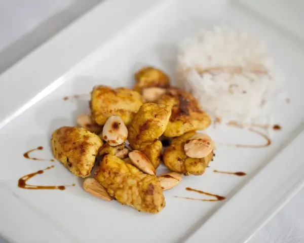 Piatto di cous cous con pollo al curry, mandorle e riso bianco.