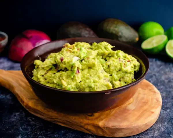 Miseczka guacamole z awokado, cebulą i limonką na drewnianej desce.