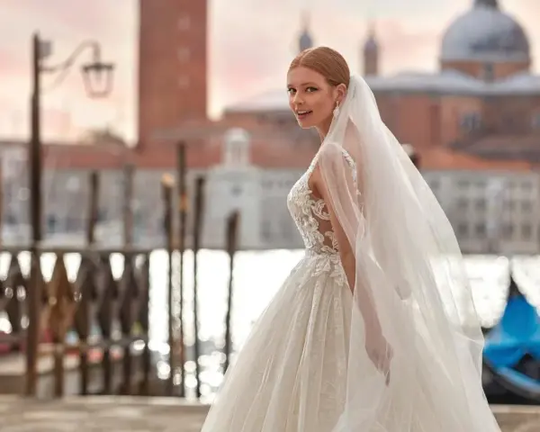 Sposa con abito da sogno e velo svolazzante a Venezia, con gondola blu sullo sfondo. Perfetta per un matrimonio da favola, anche con stivali sposa.