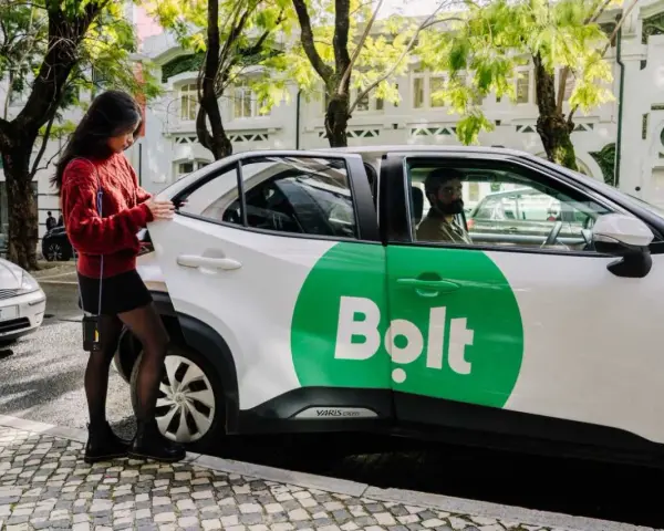Junge Frau öffnet Tür eines weißen Bolt-Taxis. Fahrer wartet.
