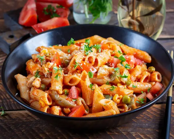 Penne w pikantnym sosie pomidorowym z kawałkami kurczaka, groszkiem i świeżymi ziołami. Danie wygląda jak pyszne spaghetti arrabiata.