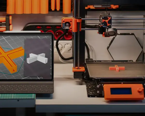 Na stole warsztatowym widać różne rodzaje drukarek 3D, tablet z modelem 3D i wydrukowany element.