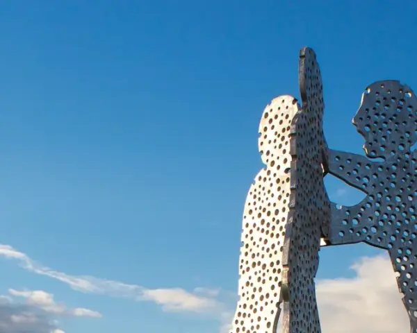 Der Molecule Man in Berlin, eine Skulptur aus Metall mit vielen Löchern, ragt gegen einen blauen Himmel mit Wolken.