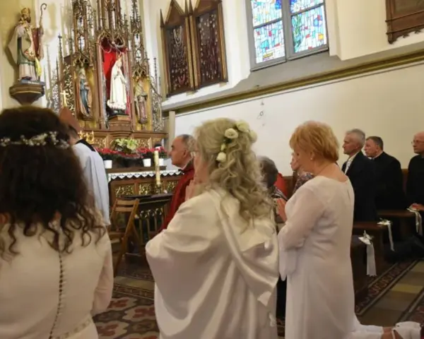 Uroczystość w kościele. Kobieta w białej sukni, z kwiatami we włosach, klęczy. To moment konsekracji, ważny dla dziewicy konsekrowanej.