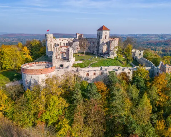 Ruiny zamku na wzgórzu, część szlaku Orlich Gniazd. Jesienne drzewa otaczają kamienne mury.