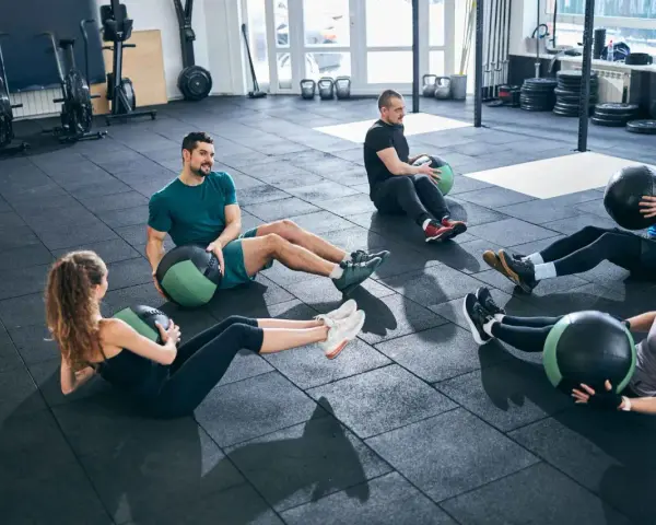 Fünf Personen machen im Fitnessstudio Sit-ups mit Medizinbällen.