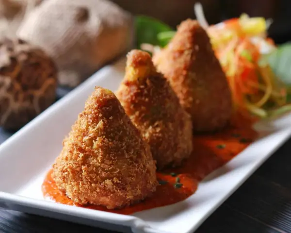 Złociste arancini, idealne do domowego arancini przepis, podane na talerzu z sosem pomidorowym i surówką.