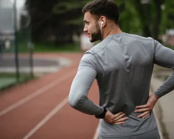 Uomo con le mani sulla schiena, che indica dolore. Forse correre fa male alla schiena, o forse è solo un momento di pausa.