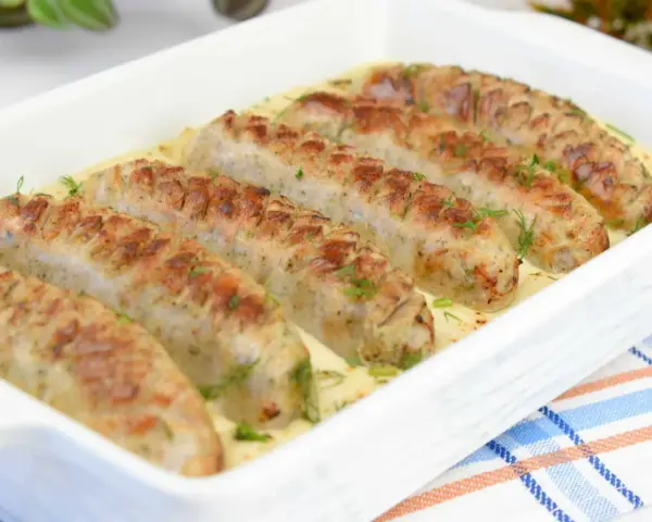 Aromaticzna biała kiełbasa w sosie chrzanowo-musztardowym, udekorowana świeżym koperkiem, podana w białej zapiekance.