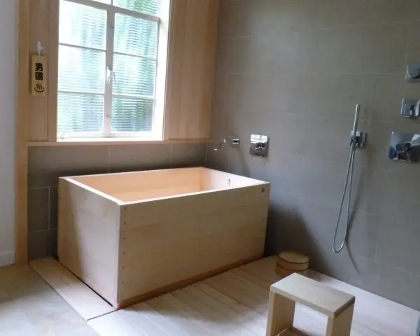 Un baño japonés con tina de madera, ducha y un pequeño taburete. El letrero de madera indica "男湯" (baño de hombres).