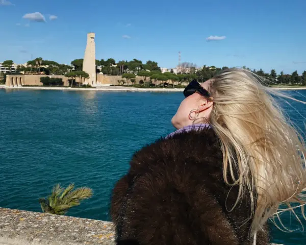 Kobieta z blond włosami podziwia pomnik i morze w Brindisi. Warto zobaczyć to miejsce!