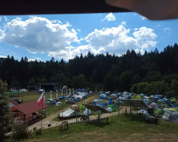 Pole namiotowe na festiwalu w Solinie. Tysiące namiotów pod błękitnym niebem z chmurami, w tle las i scena festiwalowa.