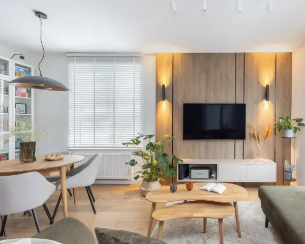 Przytulny salon inspiracje: drewniana ściana z TV, okrągły stół z krzesłami, rośliny i stylowe oświetlenie tworzą ciepłą atmosferę.