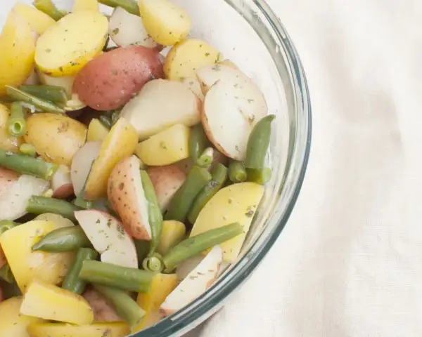 Insalata colorata di fagiolini e patate novelle, condita con erbe aromatiche, in una ciotola di vetro.