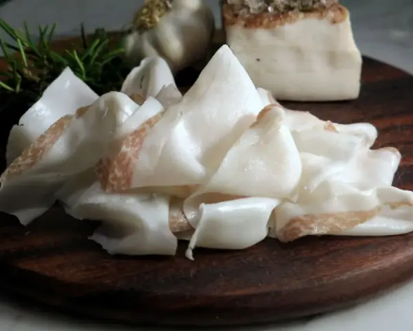 Fette sottili di lardo di Colonnata, profumate con rosmarino e aglio, pronte per essere gustate.