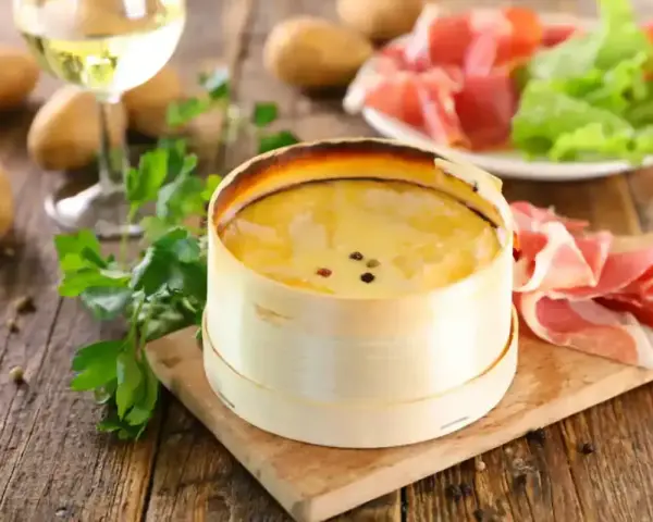 Un délicieux Mont d'Or crémeux, prêt à être dégusté avec du jambon cru, des pommes de terre et un verre de vin blanc.