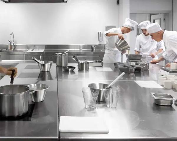 Estudiantes de cocina aprenden sobre seguridad en la cocina, preparando ingredientes en una estación de acero inoxidable.