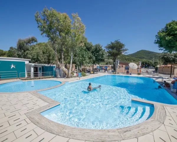 Dzieci pluskają się w basenie na terenie Miramare Camping Village. Słoneczny dzień, błękitne niebo i zieleń drzew tworzą wakacyjny klimat.