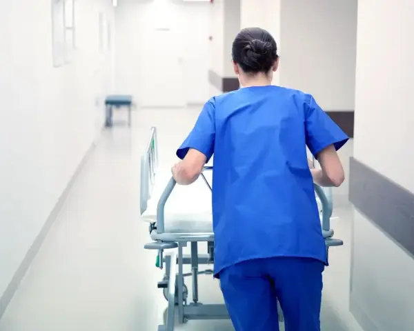Salowa w niebieskim uniformie pcha łóżko szpitalne korytarzem. To część jej obowiązków w szpitalu.