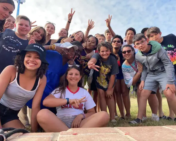 Un groupe d'enfants souriants fait un selfie en plein air, certains faisant le signe de paix.