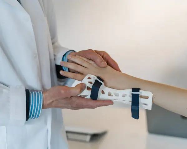 Lekarz zakłada pacjentowi ortezę na nadgarstek, co jest częścią terapii przy cieśni nadgarstka. Ćwiczenia pomogą w rehabilitacji.